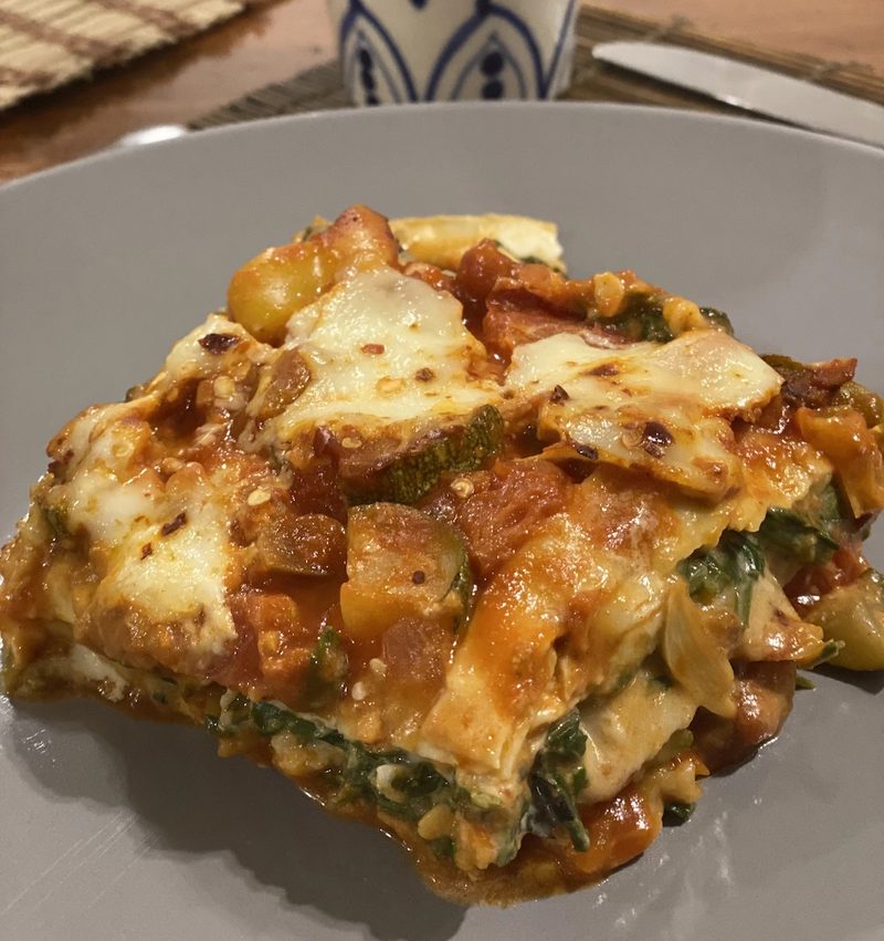 A slice of vegetable lasagna with melted mozzarella, tomato and spinach